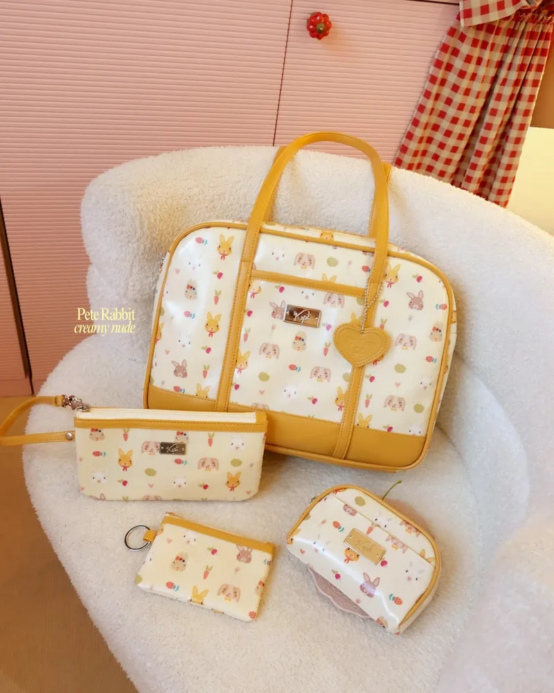 ชุดกระเป๋า The Carry Tote ลาย Pete Rabbit พร้อมกระเป๋าใบเล็ก จัดวางบนเก้าอี้ผ้าขนแกะ