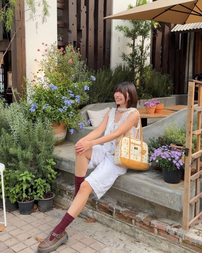 นางแบบนั่งบนขั้นบันไดสวน มีกระเป๋า The Carry Tote ลาย Pete Rabbit วางข้างตัว